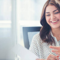 Businessman business woman working together. They are sitting at a table with a laptop computer, mobile phone and some paperwork. They are will dressed. He looks like he is talking. She is smiling, laughing and happy